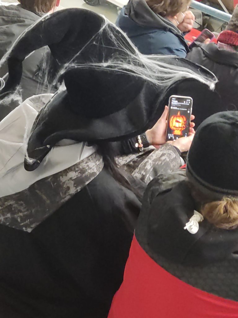 Dressed up halloween witch looking at a pumpin on a smartphone