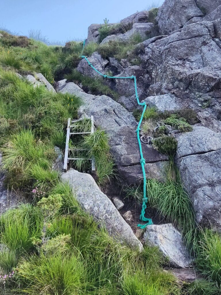 A scarily old wooden ladder (with steps partially missing) with an old rope as a handrail, for climbing up a rock on the hike.